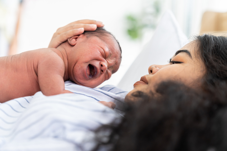 Newborn baby crying while laying with mother