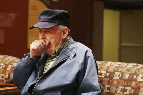 Elderly man sitting down and coughing