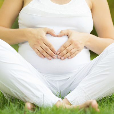 Pregnant woman sitting down with her hand on her belly in the shape of a heart