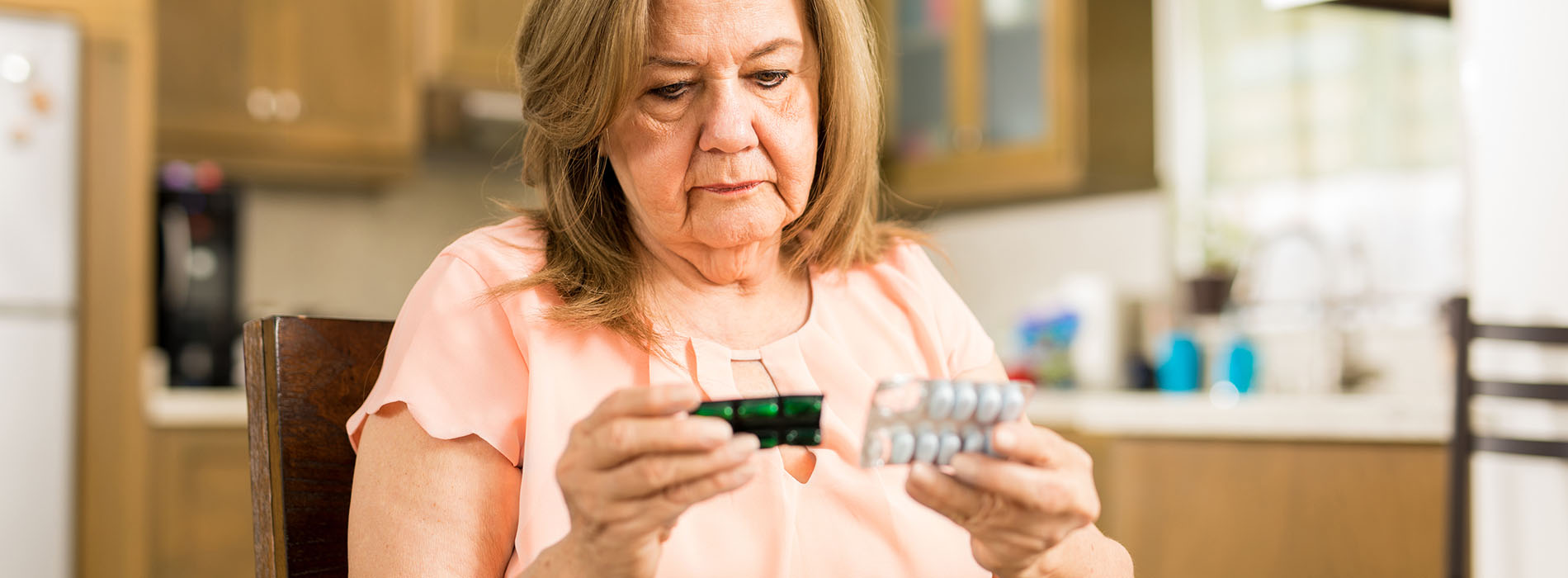 Elderly woman sitting at the table reading her medicine label